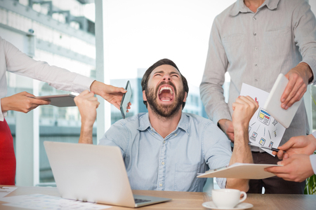 Colleagues standing by frustrated businessman at desk against working desk in a officeの写真素材