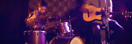 Male singer performing with drummer in illuminated nightclubの写真素材