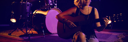 Female practicing guitar while sitting on stage in nightclubの写真素材