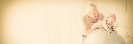 Happy mother with her baby girl in the exercice ball at home in the living roomの写真素材