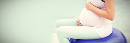 Side view of pregnant woman sitting on exercise ball next to poolの写真素材