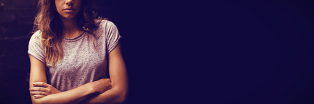 Portrait of confident young woman with arms crossed against wall