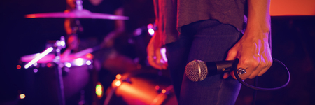 Low section of female singer holding microphone with drummer performing in illuminated nightclubの写真素材