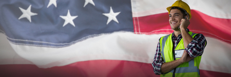 Smiling construction worker on the phone against full frame of wrinkled american flagの写真素材