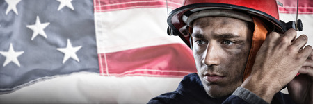 Serious Fireman putting on helmet against full frame of wrinkled american flagの写真素材