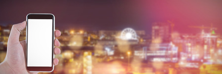 Cropped hand holding mobile phone against illuminated beautiful buildings in city