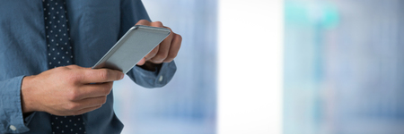 Mid-section of business man using smartphone against close-up of windowの写真素材