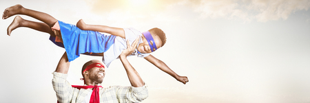 Father and son pretending to be superhero against blue sky with white cloudsの写真素材