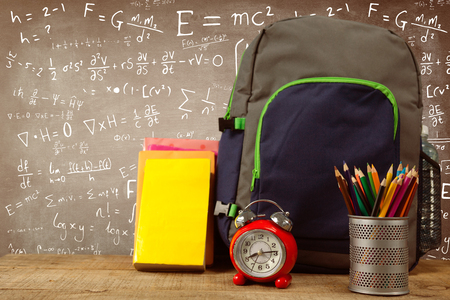 School supplies by alarm clock on wooden table against black boardの写真素材