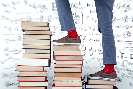 Low section of boy climbing stack of books against mathsの写真素材