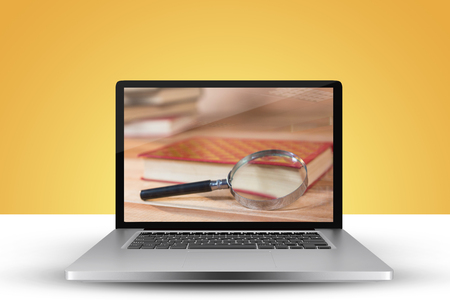 Laptop with with screen against magnifying glass with book on tableの写真素材
