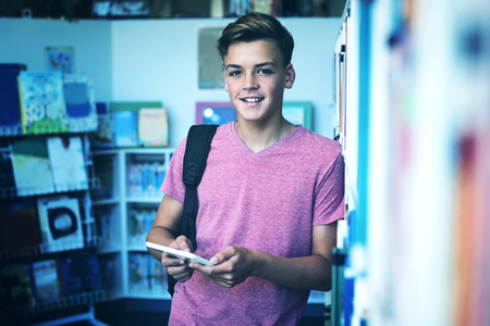 Portrait of happy schoolboy holding digital tablet in library at schoolの写真素材