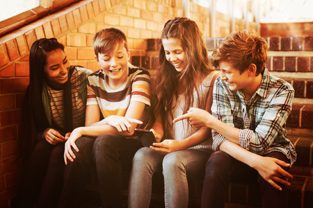 Smiling school students sitting on the staircase using mobile phone at schoolの写真素材