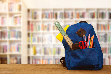 Schoolbag on wooden table against teacher reading books to her studentsの写真素材