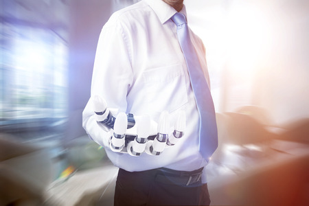Midsection of businessman with robotic hand against empty table and chair in waiting area of officeの写真素材