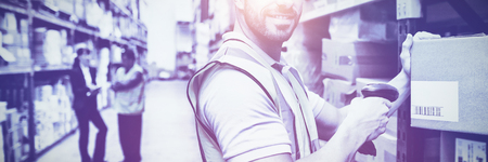 Warehouse worker scanning box while smiling at camera in a large warehouseの写真素材