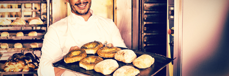 Happy baker showing tray of fresh bread in the kitchen of the bakeryの写真素材