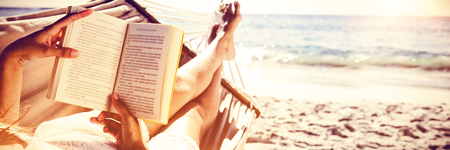 Brunette reading book while relaxing on hammock at the beachの写真素材