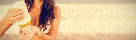 Sexy young brunette on the beach taking care of her body putting on sun cream