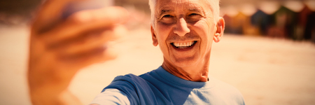 Happy senior man taking selfie at beach during sunny day