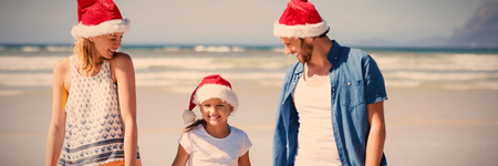 Happy family wearing Santa hat while standing at beach during sunny dayの写真素材