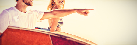 Happy man with woman gesturing while carrying sunrfboard at beach during sunny dayの写真素材