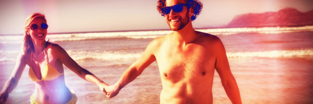 Happy couple holding hands while enjoying at beach during sunny dayの写真素材