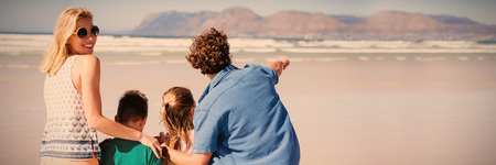 Smiling woman standing with her family at beach during sunny dayの写真素材