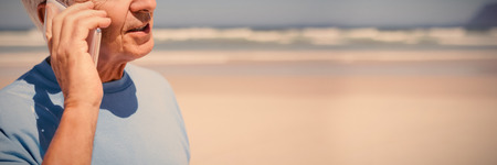 Senior man talking on mobile phone at beach during sunny dayの写真素材