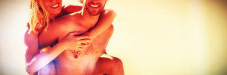 Portrait of young man piggybacking beautiful woman at beach during sunny dayの写真素材