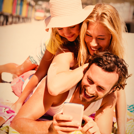 Happy family taking selfie while lying on picnic blanket at beach during sunny dayの写真素材