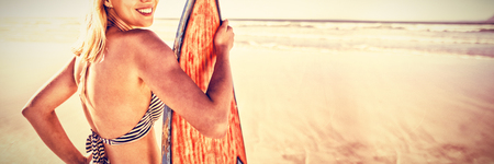 Portrait of smiling woman holding surfboard at beach during sunny dayの写真素材