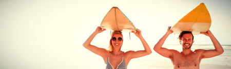 Portrait of happy couple carrying surfboard at beach during sunny day