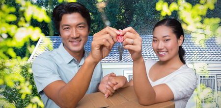 Happy couple holding house key and leaning on moving box against pretty house with a blue and white...