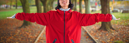 Smiling woman standing with arms outstretched against footpath amidst trees at park
