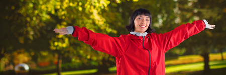Smiling woman standing with arms outstretched against trees growing at parkの写真素材