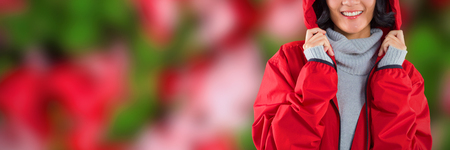 Smiling woman in hooded jacket standing against white background against maple leaves fallen on grassの写真素材