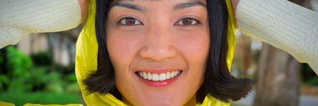 Woman wearing yellow raincoat against white background against footpath by trees in city