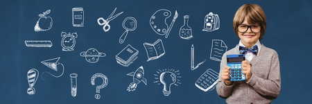 Digital composite of School boy holding calculator and Education drawing on blackboard for school