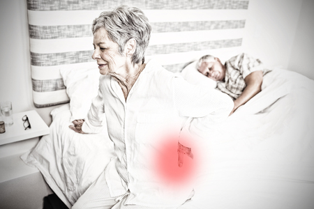 Highlighted pain against senior woman suffering from backache sitting on bedの写真素材