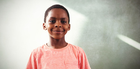 Portrait of smiling boy holding cellphone while standing against greenboard in school