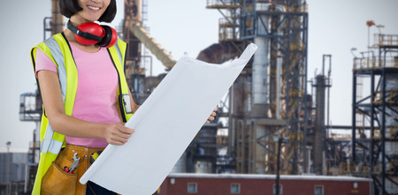 Female architect holding blueprint against white background against image of factory