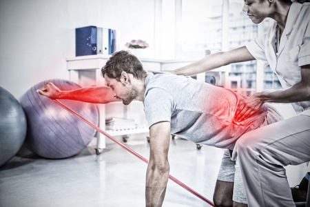 Highlighted pain against female physiotherapist assisting a male patient while exercisingの写真素材