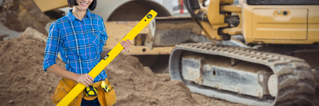 Female architect holding measuring equipment against grey background against bulldozer at...