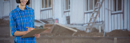 Female architect writing on clipboard against grey background against mud and construction materialsの写真素材