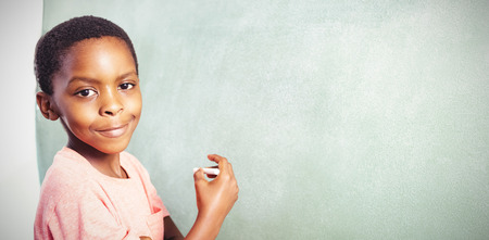 Portrait of boy standing by greenboard in classroom