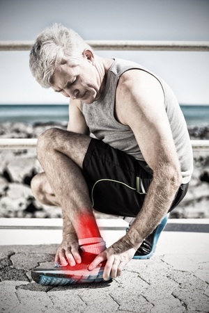 Highlighted pain against fit man gripping his injured ankleの写真素材