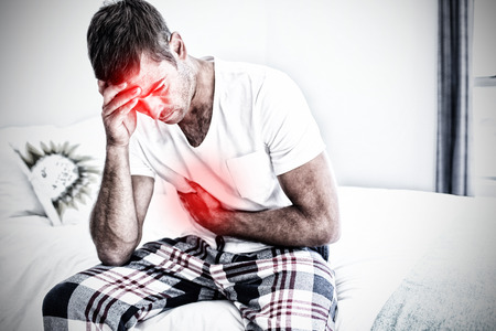 Highlighted pain against young man sitting with stomach pain on bedの写真素材
