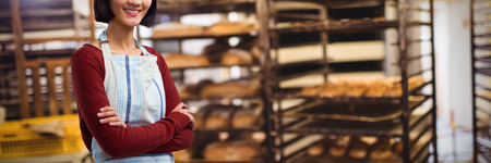 Smiling waitress standing with arms crossed against white background against baking trolley in...