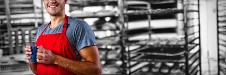 Male waiter holding coffee mug against baking trolley in bakery shopの写真素材